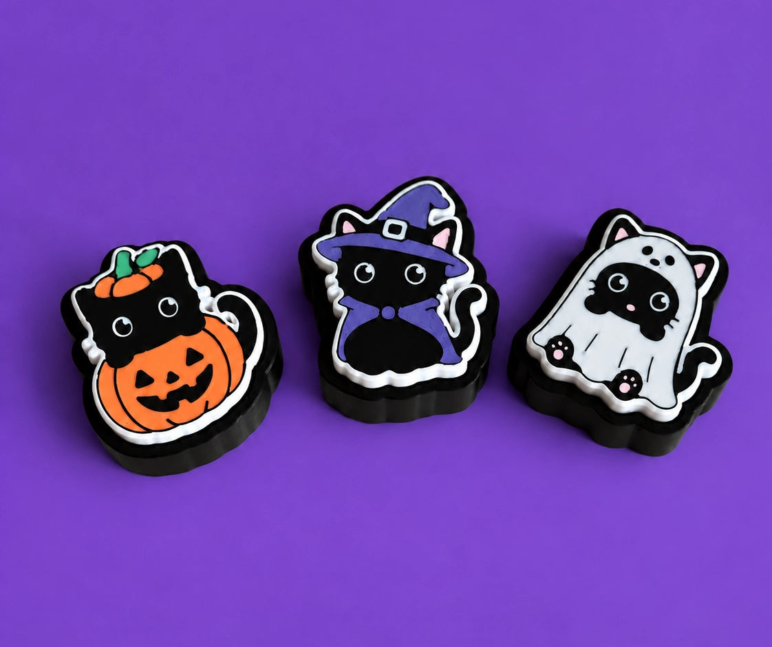 Die drei Halloween-Kätzchen-Schlüsselanhänger-Clicker zusammen: Kürbis, Hexe und Geist, vor violettem Hintergrund - Kokoroto