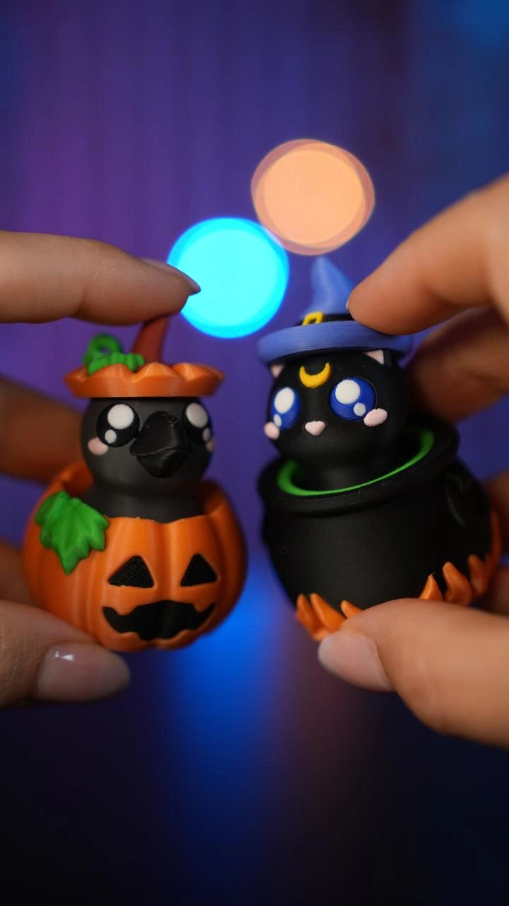 Hände halten zwei Halloween-Schlüsselanhänger-Clicker: einen in Kürbisform und einen als Kessel mit Hexenkätzchen - Kokoroto