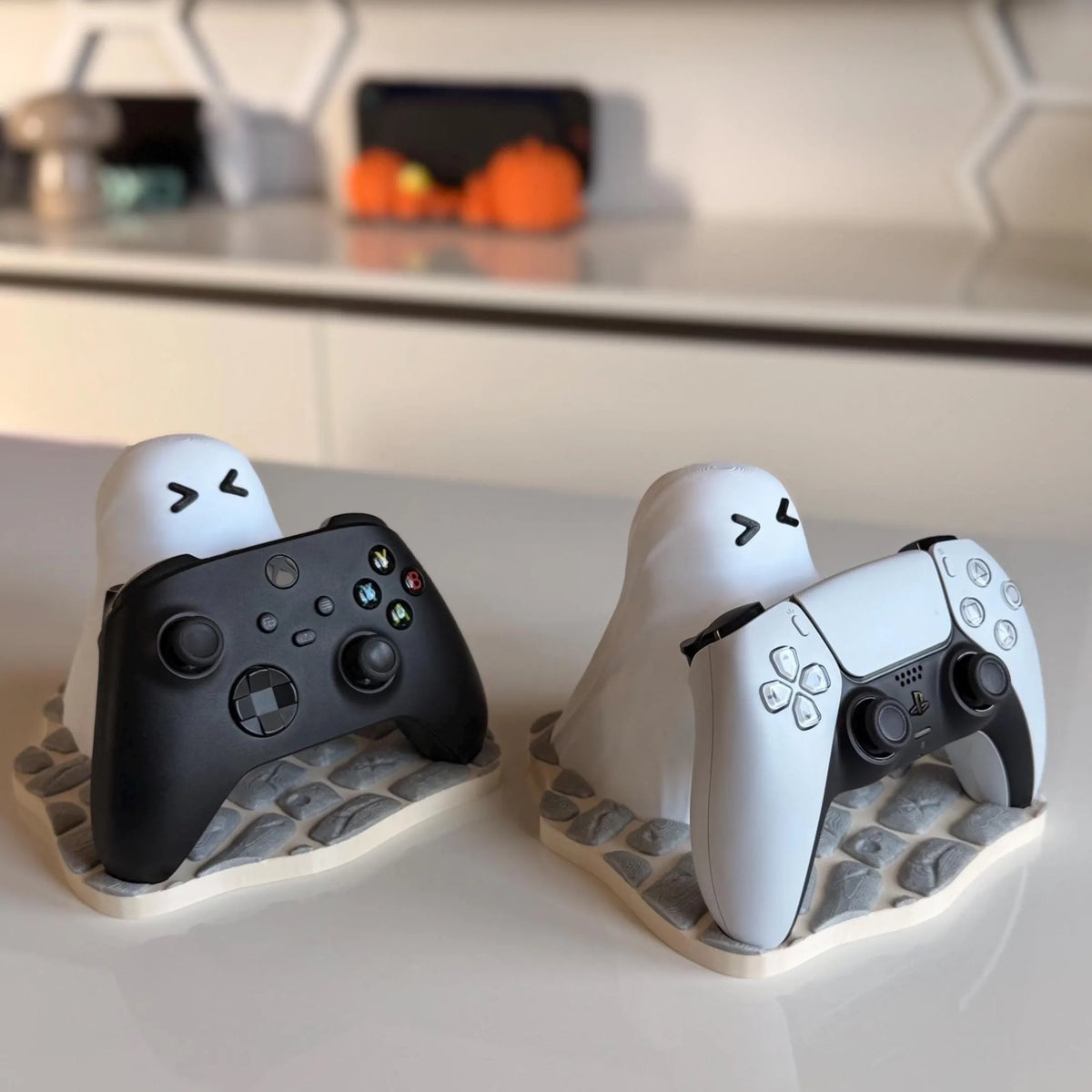 Soporte Ghost Buddy con mando Xbox y PS5, sobre una encimera con calabazas decorativas de fondo - Kokoroto