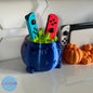 Witch's cauldron for Joy-Con in metallic blue with the turquoise and red controllers placed inside the green interior - Kokoroto