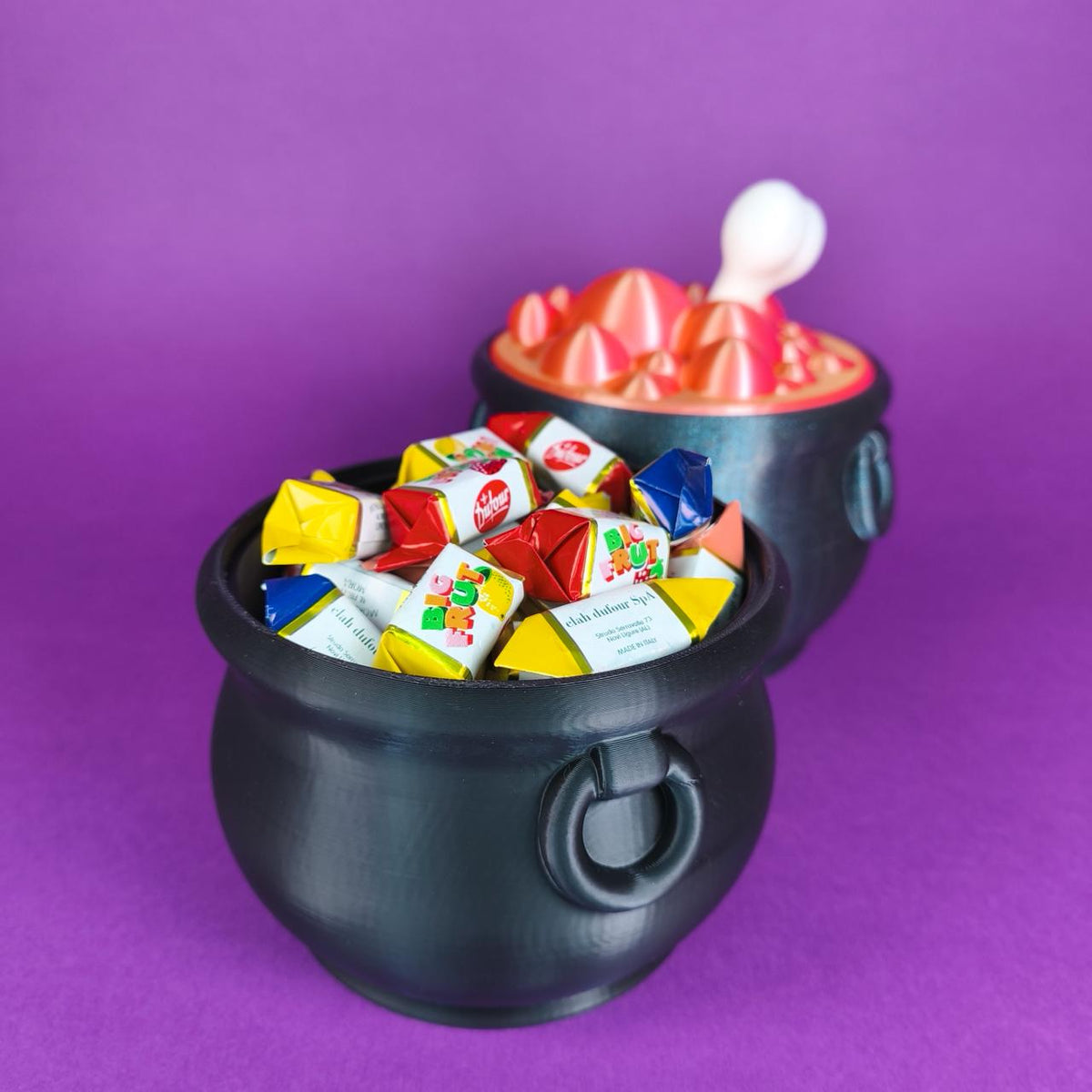 Caldero de bruja para caramelos relleno de caramelos envueltos de verdad, con el otro caldero de poción rosa al fondo - Kokoroto